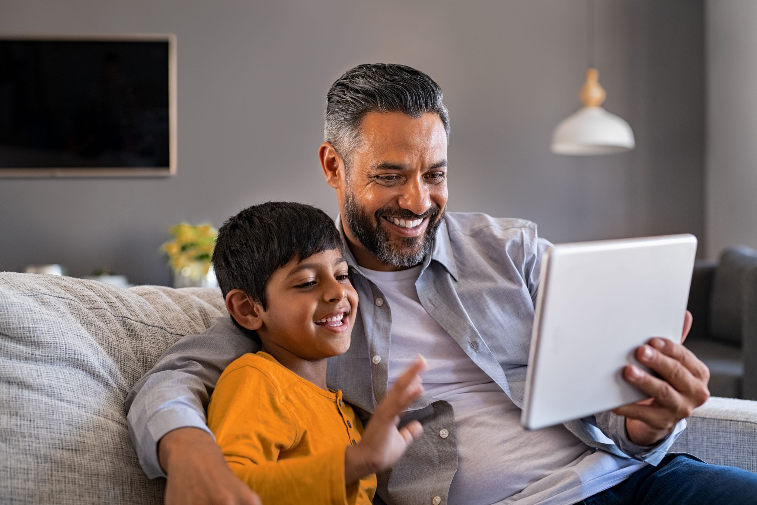 Father and Son with Tablet A father and son seating on their couch, the dad is holding up a tablet and they are both looking at the tablet screen